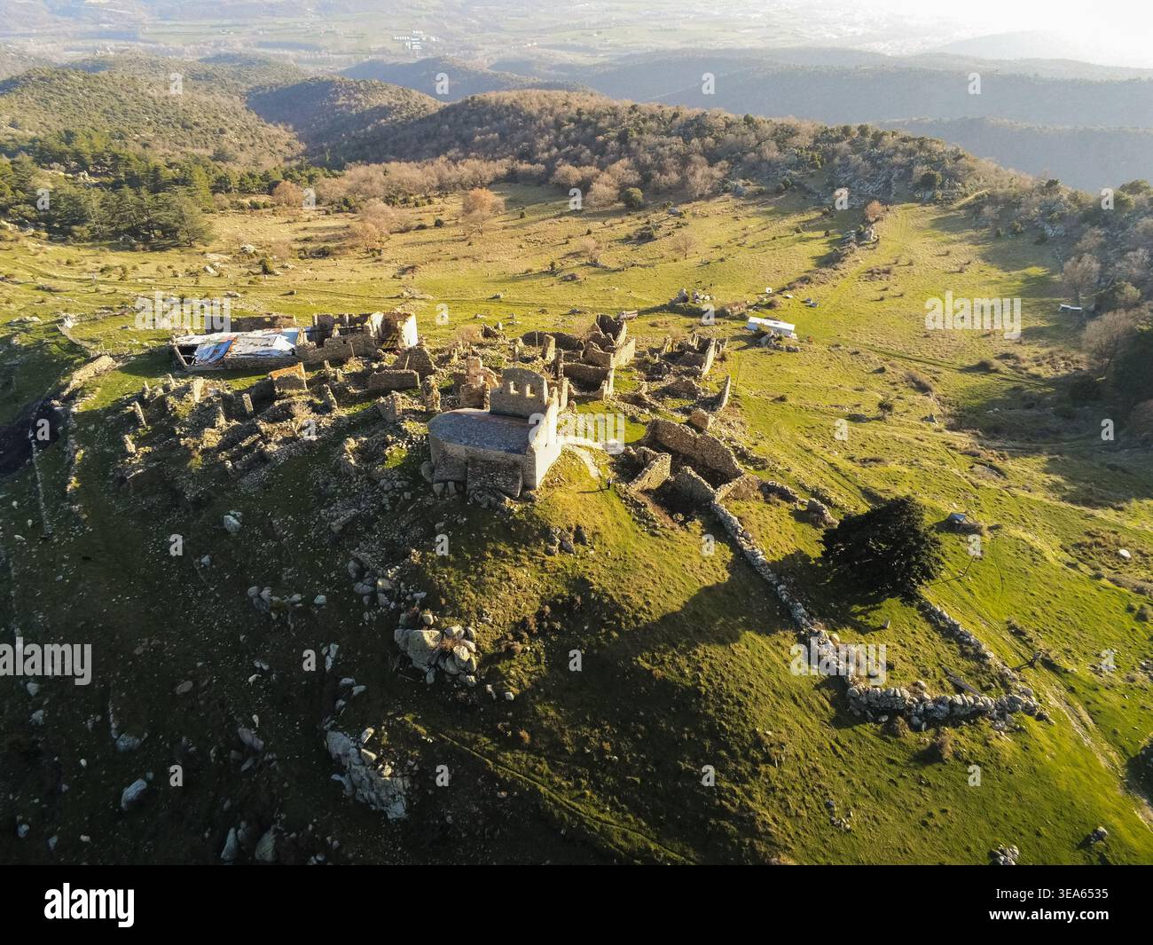 Veduta aerea delle antiche rovine di pietra del villaggio abbandonato di arriva su una collina erbosa a EUS, Occitanie, Francia. Foto Stock