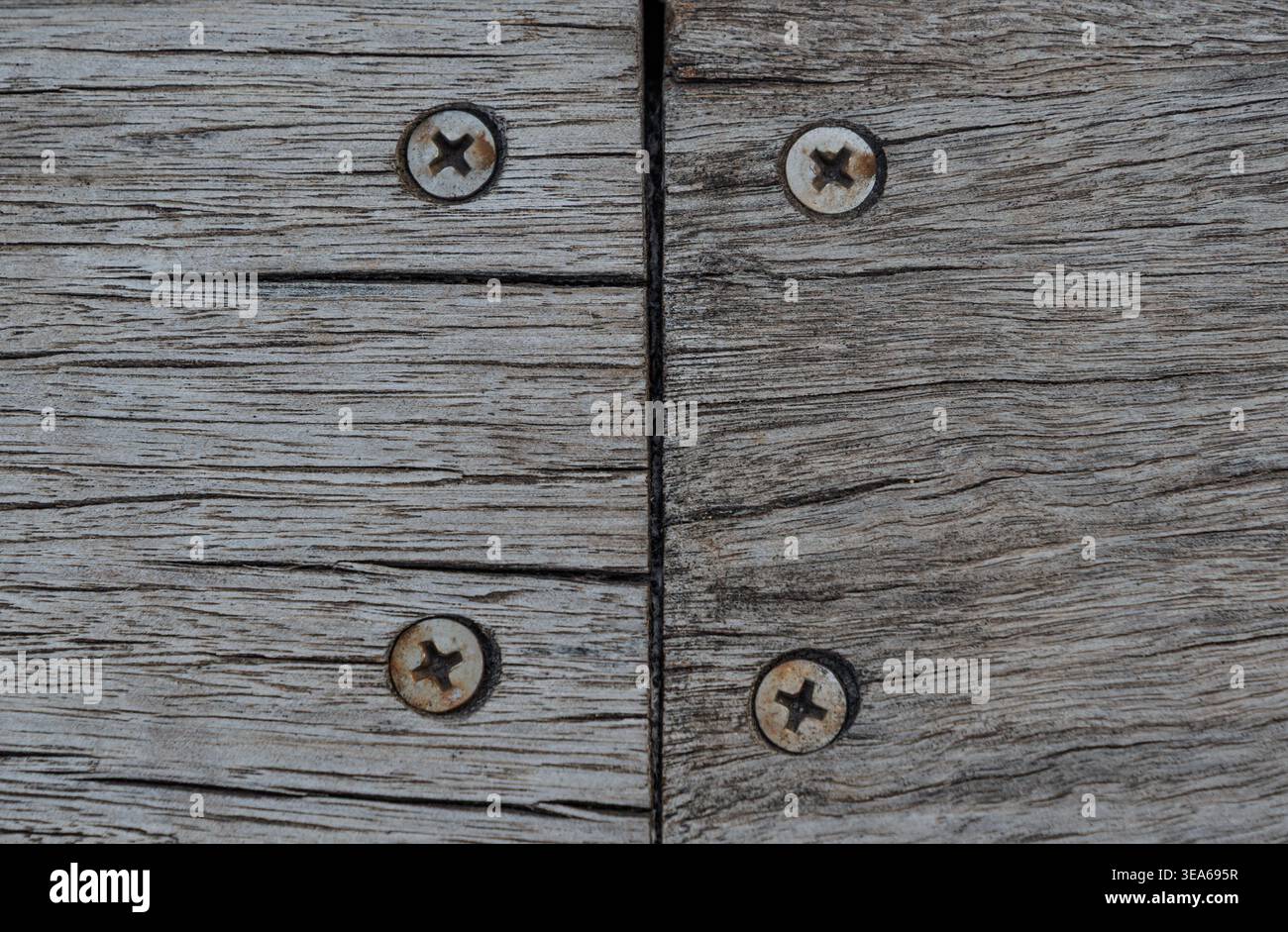 Quattro viti in metallo arrugginito fissano insieme tavole in legno grigio ruvido e ruvido creando una superficie robusta Foto Stock