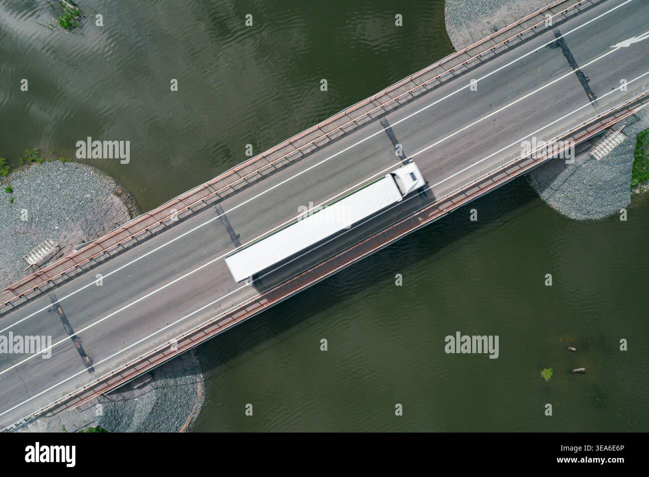 Il semirimorchio bianco attraversa un lungo ponte di cemento che attraversa un fiume verde scuro. Foto Stock