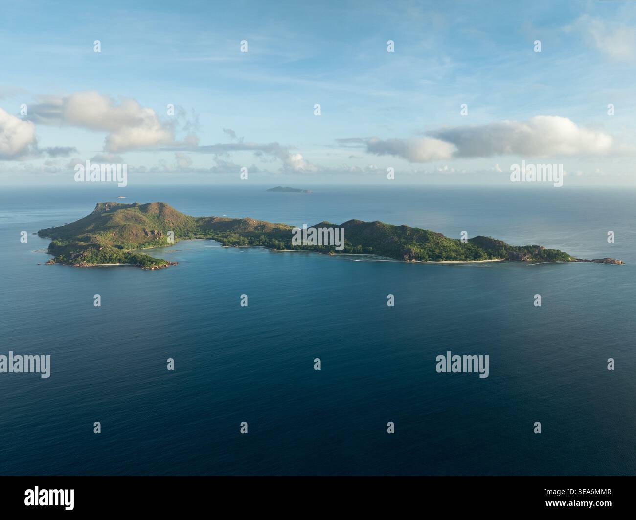 Vista aerea dell'isola di Praslin con lussureggianti colline verdi e spiagge di sabbia bianca circondate dal turchese Oceano Indiano sotto un cielo blu con morbide nuvole Foto Stock