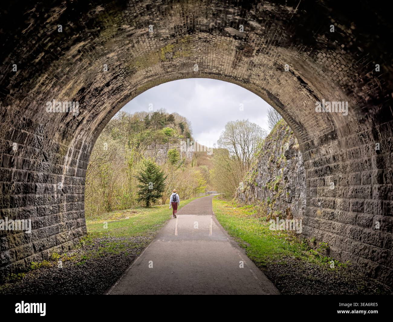 Veduta posteriore di una camminatrice che esce dal tunnel ferroviario in disuso sul Monsal Trail, Peak District National Park, Derbyshire, Inghilterra, Regno Unito Foto Stock