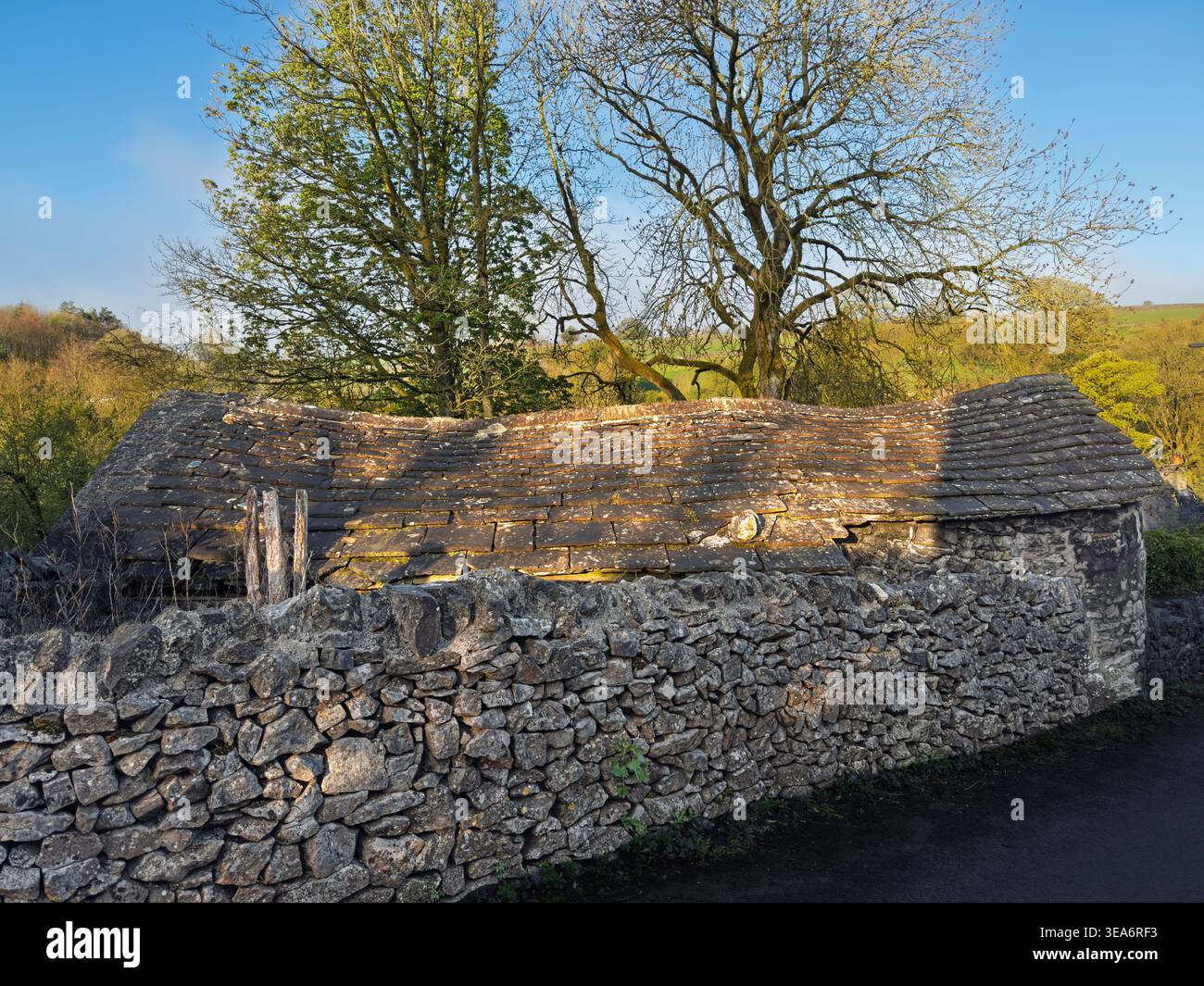 Edificio in pietra con tetto in ardesia di pietra cedevole dietro il muro di pietra a secco a Tideswell, Peak District National Park, Derbyshire, Inghilterra, Regno Unito Foto Stock