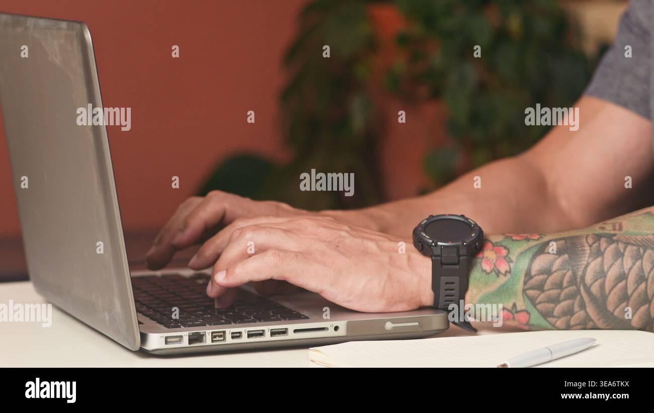 Digitazione tatuata sul laptop nel moderno spazio di lavoro remoto con smartwatch e notebook Foto Stock