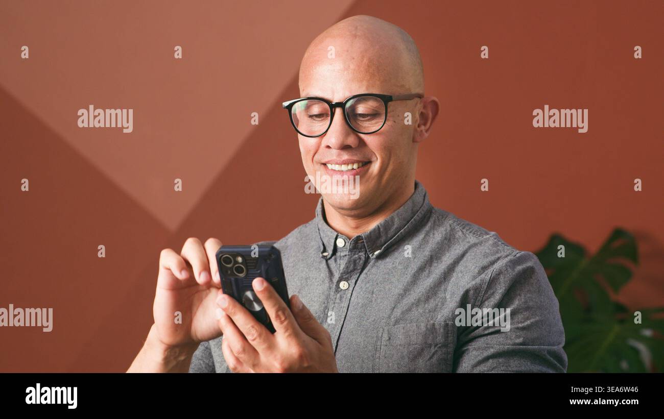 Uomo d'affari sorridente che utilizza lo smartphone in ambiente ufficio informale per lavoro e comunicazione in remoto Foto Stock