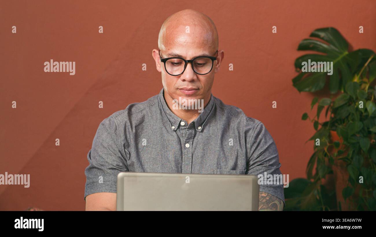 Uomo calvo con occhiali che lavora su un notebook con un'elegante impostazione di lavoro remoto per ufficio domestico Foto Stock