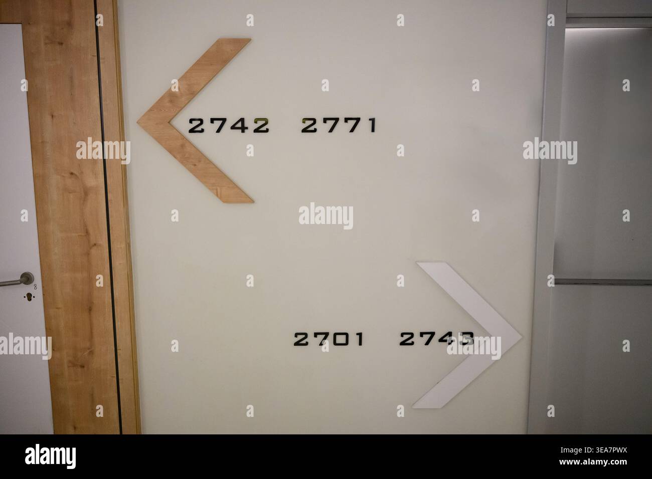 Moderno cartello con i numeri delle camere d'albergo con frecce sulla parete bianca, sistema di navigazione minimalista nel corridoio dell'edificio, affitto di uffici, camera d'albergo. Design degli interni e concetto di architettura. Navigazione chiara Foto Stock