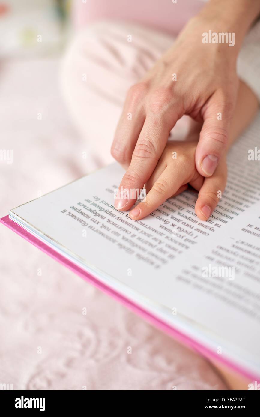 Genitore e bambino mette le mani su un libro aperto, che indica il testo, illustra l'educazione, l'apprendimento e il legame della prima infanzia Foto Stock