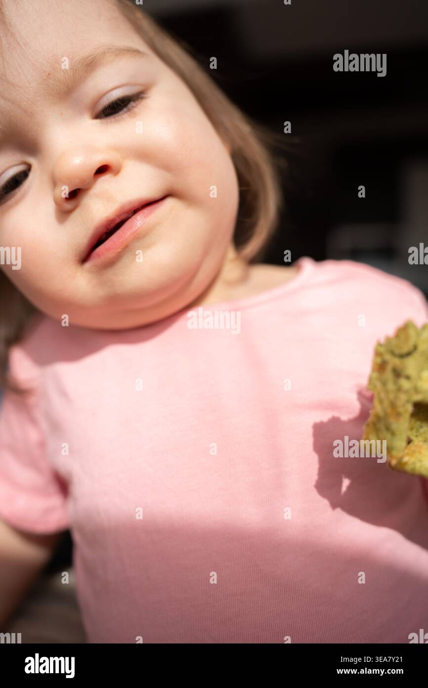 primo piano ritratto di un bambino al chiuso che indossa una camicia rosa tenue, luce solare calda e ombre delicate sulla guancia e sul mento mentre il bambino tiene in mano una c Foto Stock