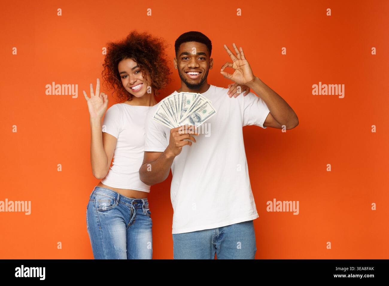 Allegra coppia afro-americana che mostra segni buoni con un mucchio di soldi Foto Stock