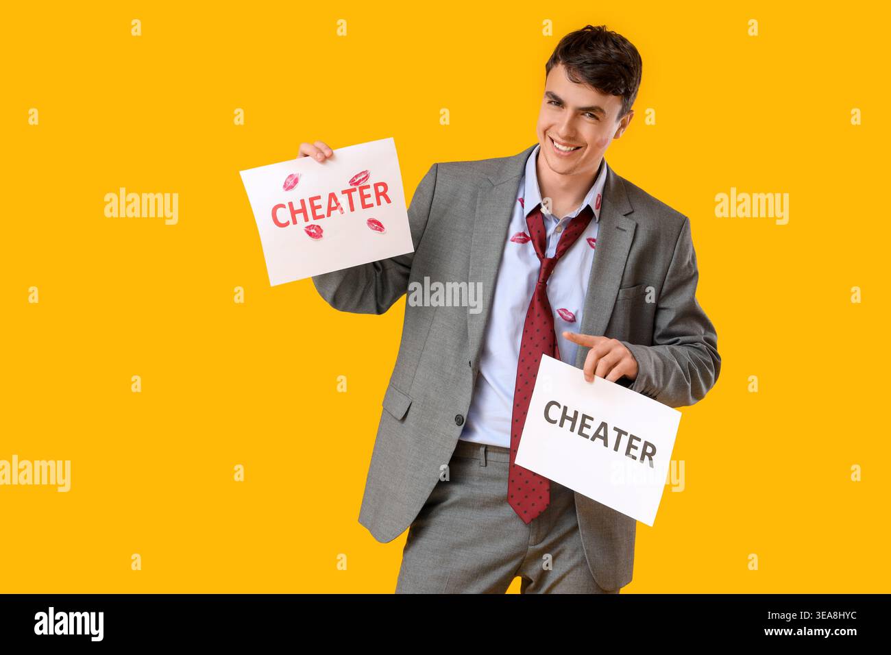 Uomo felice con segni di bacio sulla sua camicia che regge fogli di carta con IMBROGLIONE su sfondo giallo Foto Stock