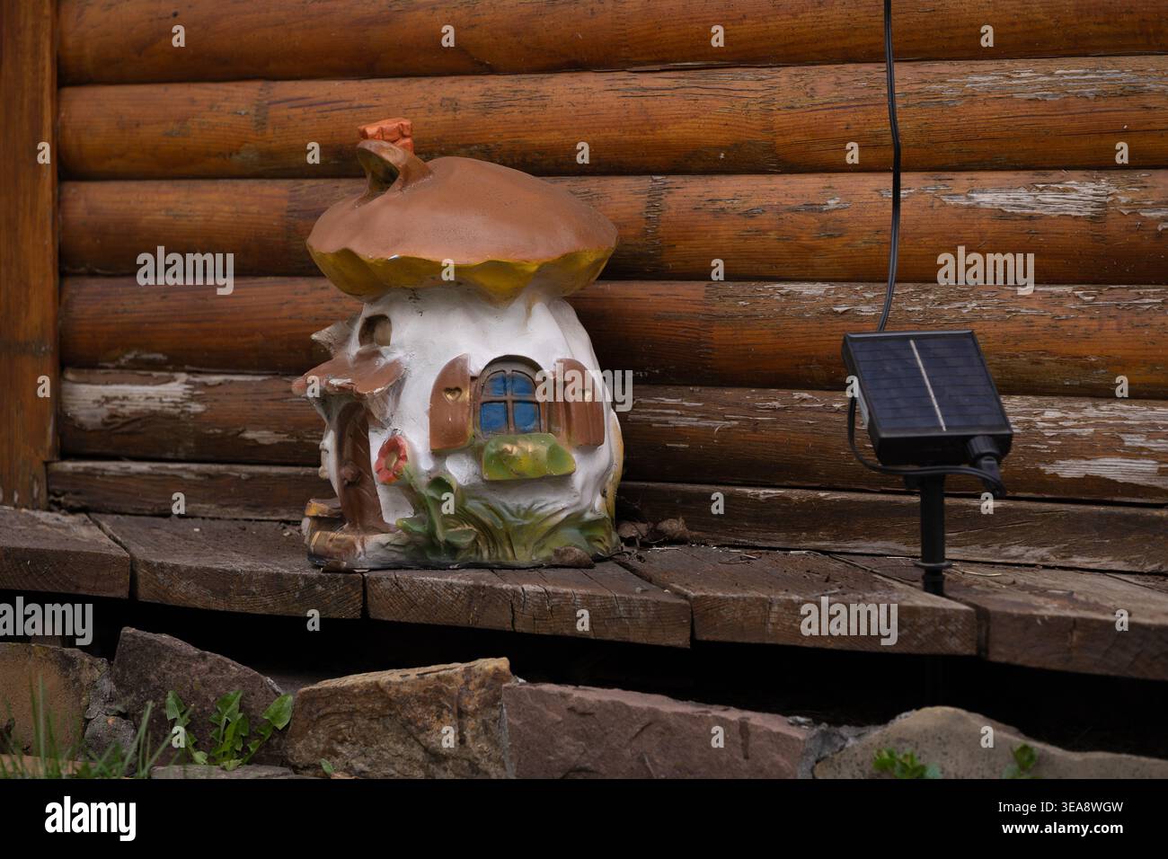 Fantasiosa statuetta per la casa dei funghi con luce solare sullo sfondo rustico delle pareti della cabina in legno intempestivo. Foto Stock