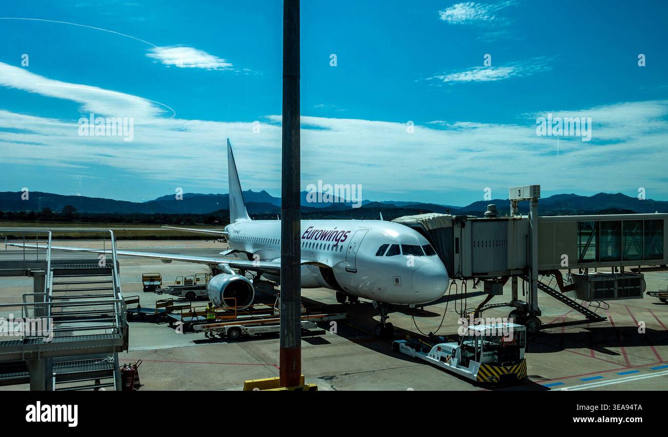 Eurowings Airbus A320 presso l'aeroporto Costa Smeralda di Olbia, Italia. L'aereo è attraccato su un jet bridge sulla soleggiata asfalto con montagne in lontananza. Foto Stock