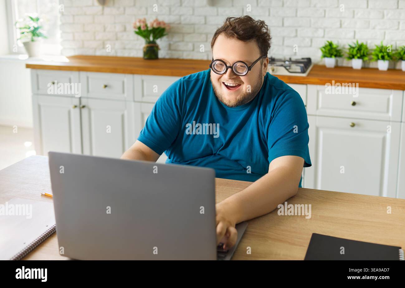 Allegro uomo di grandi dimensioni che si diverte online a casa, sorridendo mentre usa il notebook Foto Stock