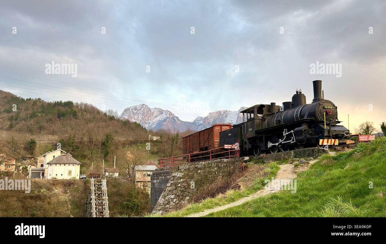 Locomotiva a vapore d'epoca con carri merci nel paesaggio montano della campagna al tramonto. Trasporto ferroviario storico e ambiente rurale panoramico. - Immagine stock catturata con smartphone