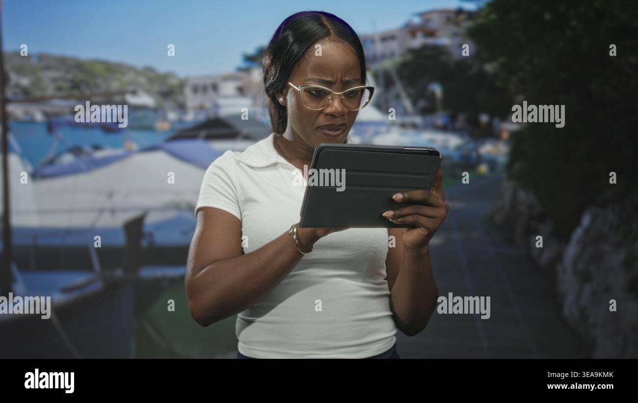 Donna che tiene in mano un tablet e sta girovagando mentre legge con le dita sullo schermo in uno studio con sfondo porticciolo e oggetti di scena del molo; attenzione all'esame. Foto Stock