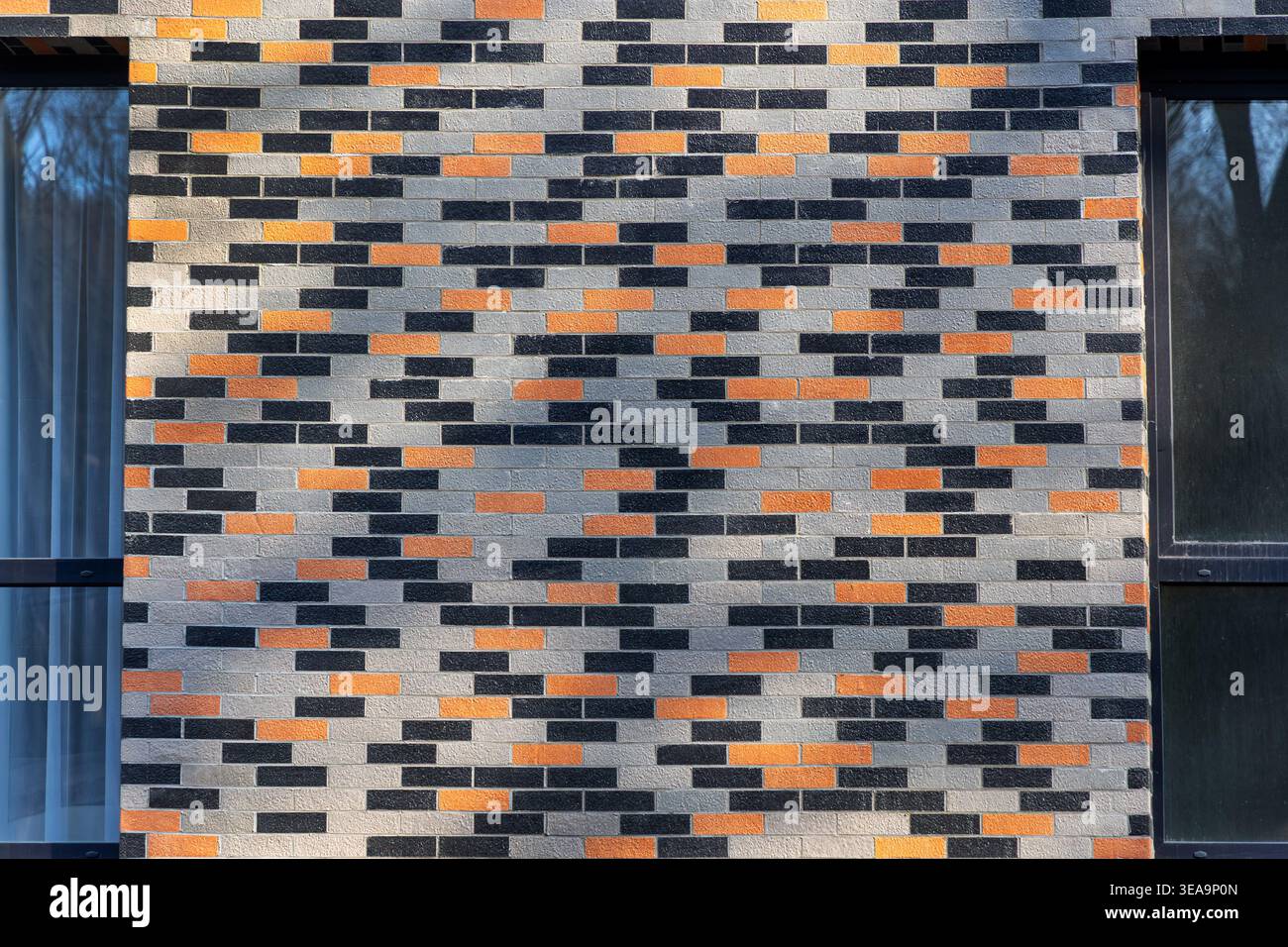 Moderna facciata in mattoni a motivi geometrici. Vista frontale di una parete contemporanea in mattoni con blocchi grigi, neri e arancioni che creano una forma geometrica Foto Stock