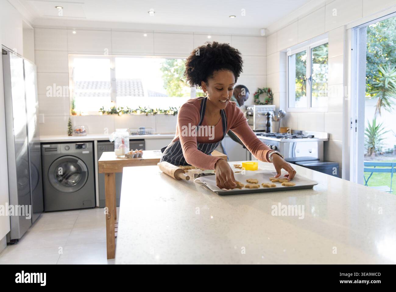Una coppia afroamericana che cuoce, una donna che mette l'impasto su una teglia da forno in cucina con grembiule Foto Stock