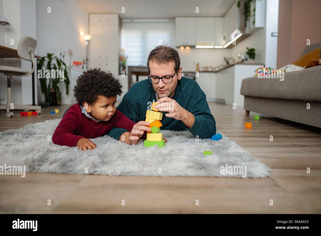 Padre e figlio costruiscono blocchi di giocattoli colorati insieme su un tappeto Foto Stock