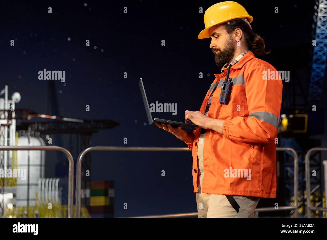 I dipendenti della piattaforma offshore monitorano le operazioni utilizzando un computer portatile sul ponte della piattaforma petrolifera a tarda notte. Tecnico chiatte che indossa un elmetto per rivedere le operazioni energetiche su un carro di perforazione utilizzando un notebook Foto Stock