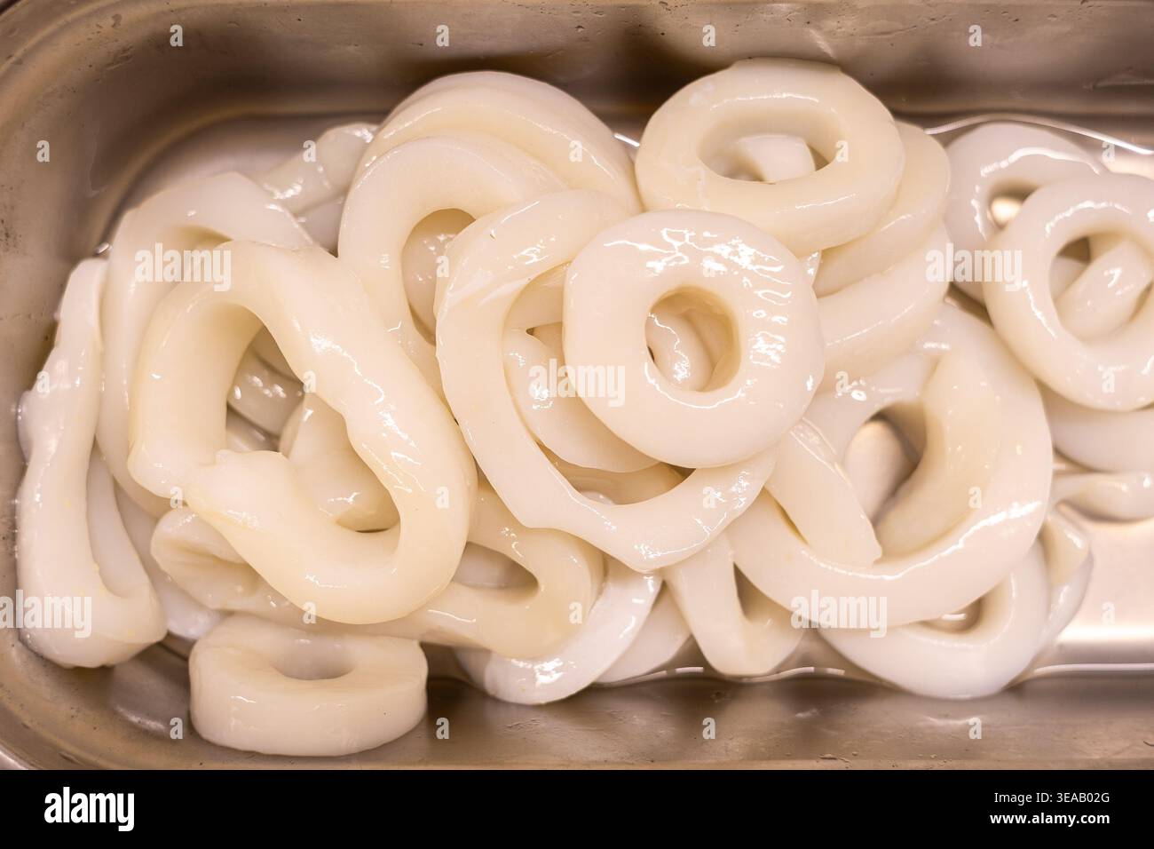 Un vassoio può contenere più anelli di calamaro freschi in un mercato di pesce. Gli anelli sono lucenti e pronti per la vendita. Questo display mostra i frutti di mare pronti per la cottura Foto Stock