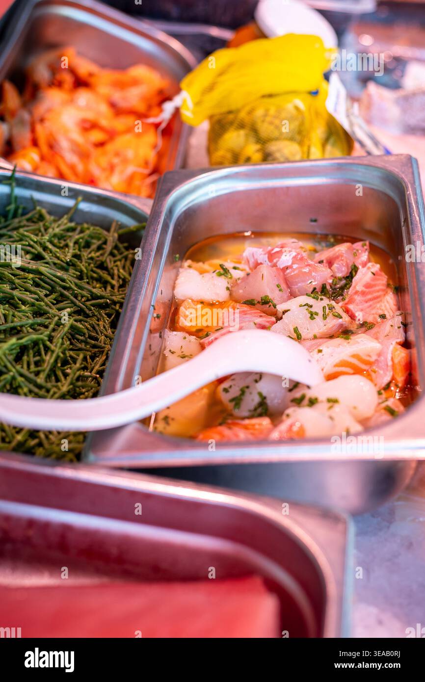 I gamberetti e altri frutti di mare sono esposti in vassoi in un mercato. Piante verdi e barattoli di condimenti sono collocati nelle vicinanze, creando una vivace scena del mercato Foto Stock