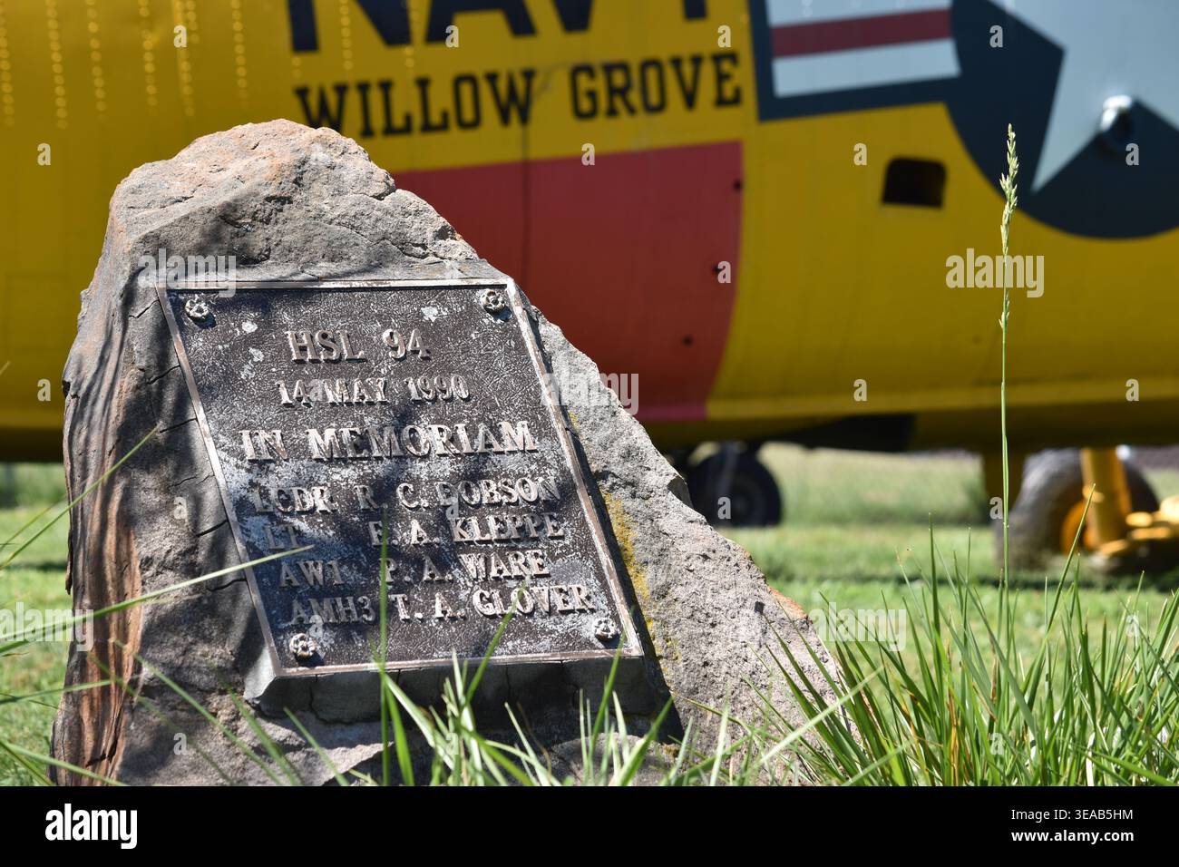 Targa commemorativa in pietra e bronzo che commemora quattro membri dell'equipaggio della US Navy HSL-94 persi il 14 maggio 1990, situata su terreni erbosi con un aereo giallo. Foto Stock
