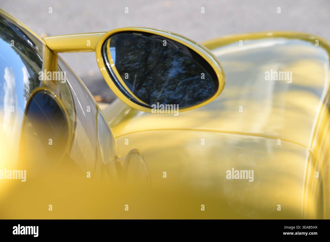 Dettaglio ravvicinato di un'auto gialla ultima SS che mostra lo specchio laterale ovale e la carrozzeria lucida con riflessi sugli alberi in una mostra di auto all'aperto. Foto Stock