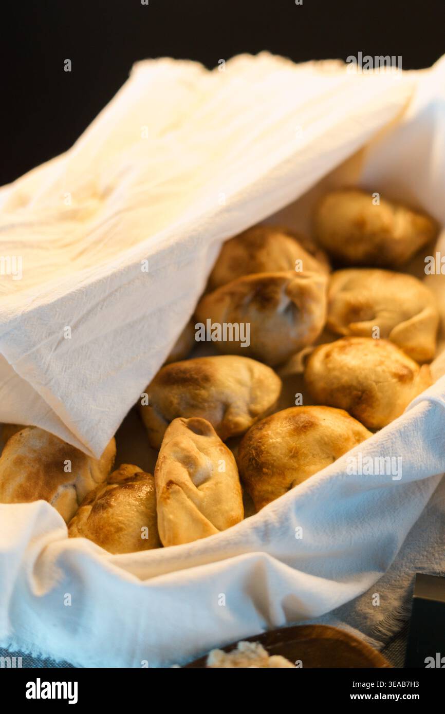 I panini dorati riposano in un cestello bianco rivestito in tessuto. L'illuminazione calda mette in risalto le croste croccanti. La carta assorbente si piega delicatamente sulla parte superiore. Clos Foto Stock