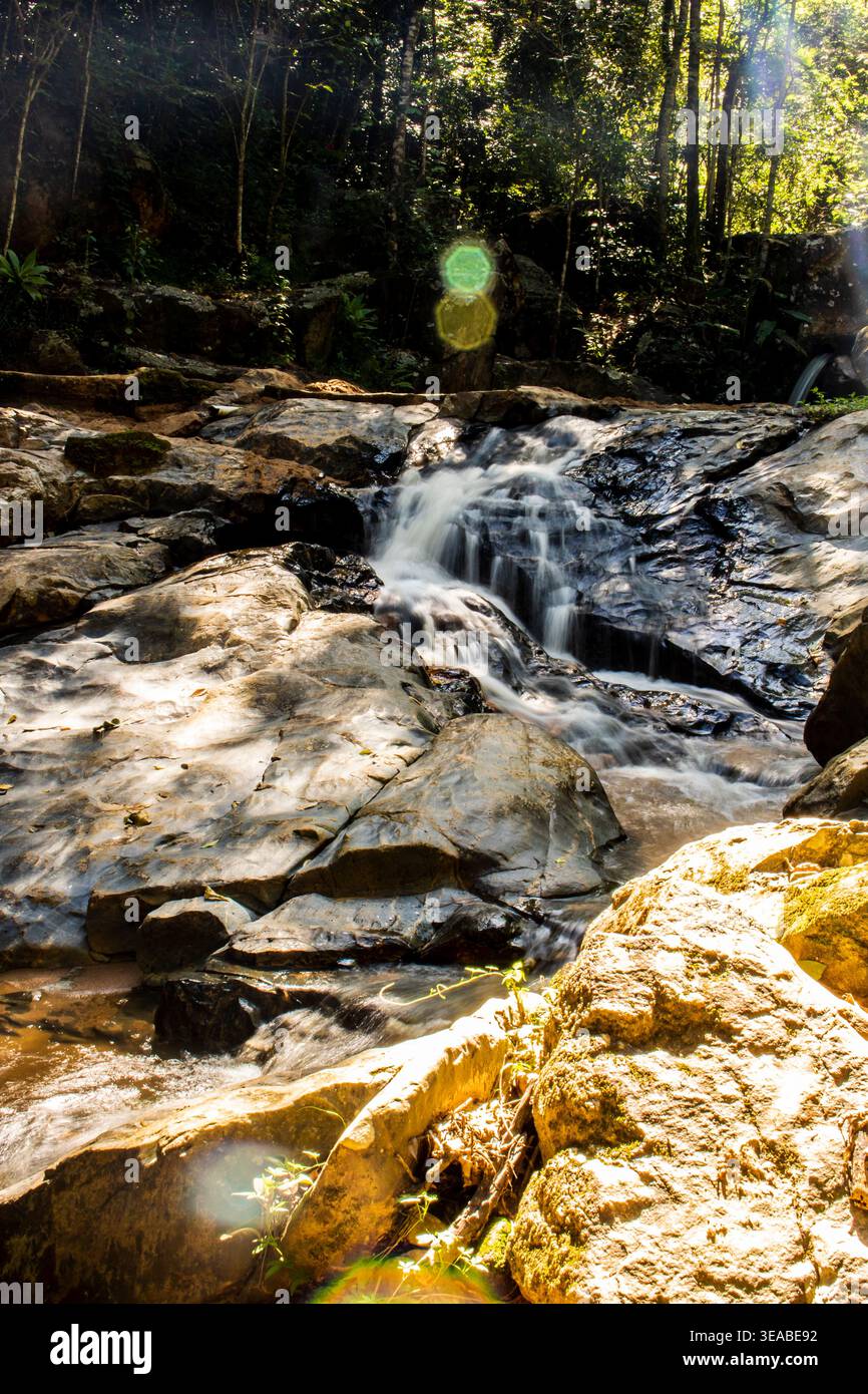 Una piccola e serena cascata si innalza su rocce scure e scintillanti in un flusso continuo e delicato, catturando la pura e cruda bellezza della natura in movimento a Bra Foto Stock