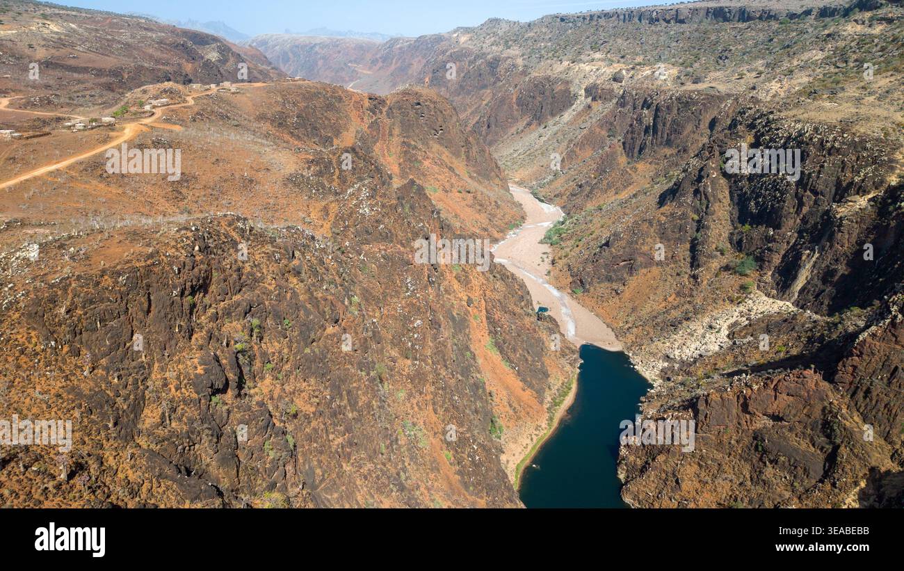 Vista aerea dell'aspro canyon del deserto con ripide scogliere rocciose e un tortuoso bacino idrico sottostante sotto la luce del sole, che mostra un paesaggio arido e remoto Foto Stock
