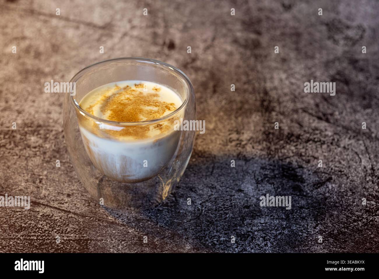 Vista laterale del caffè sporco in vetro a doppia parete su un tavolo in cemento scuro. Loft industriale in stile caffetteria con una suggestiva illuminazione laterale. Foto Stock