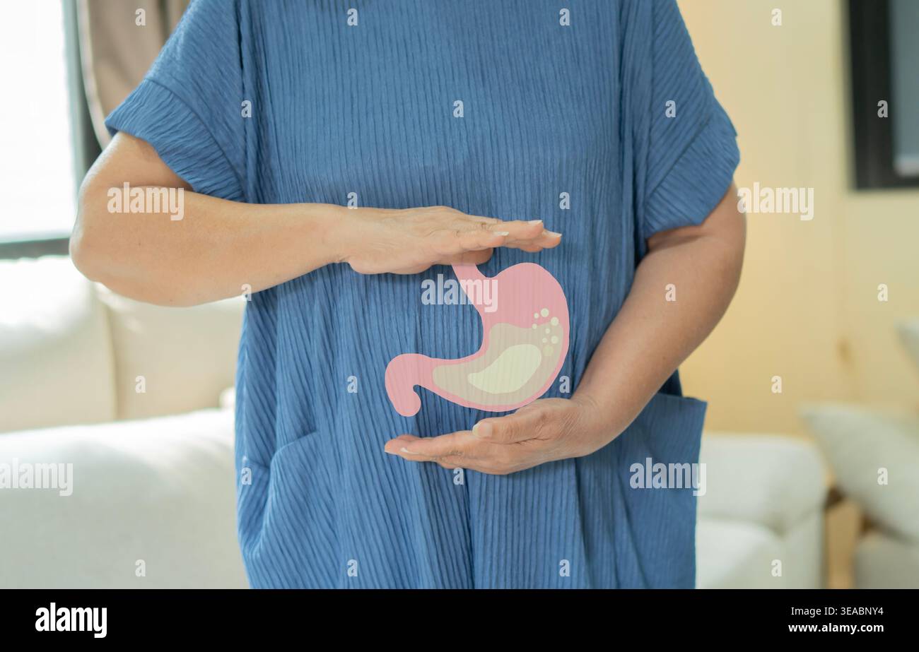 Donna anziana con stomaco che sente dolore o gastrico mentre è in piedi a casa. Senior che soffre di problemi di digestione o reflusso acido. Foto Stock