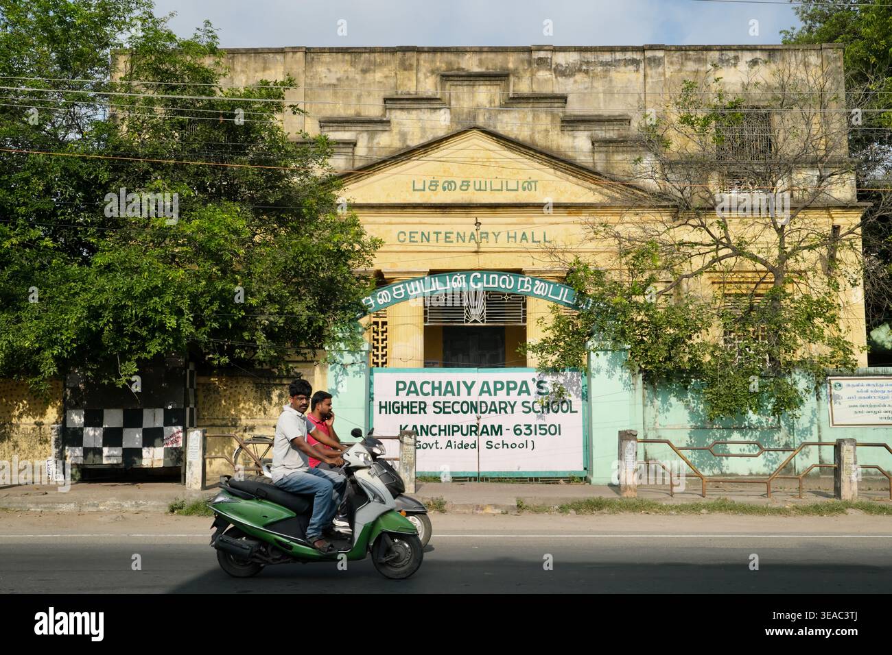 I motociclisti che passano davanti alla Centenary Hall e una scuola situata all'interno dell'edificio, la Panchaiyappa's Secondary School; Kanchipuram, Tamil Nadu, India meridionale Foto Stock