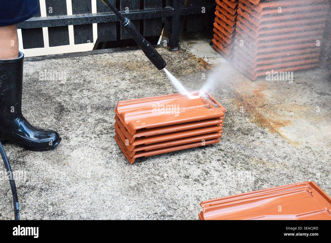 Un primo piano ad angolo alto che mostra una persona che utilizza un getto d'acqua ad alta pressione per pulire una pila di tegole rosse tradizionali di argilla su una truffa Foto Stock