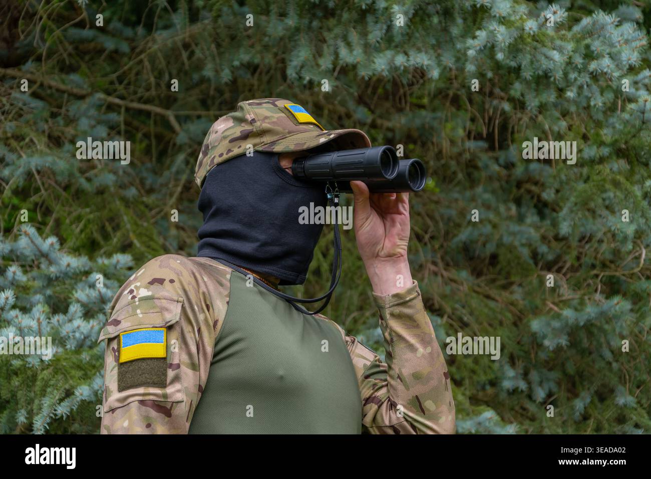 Soldato con patch Ucraina guardando attraverso binocoli sorveglianza ricognizione controllo rischio di sicurezza. Foto Stock