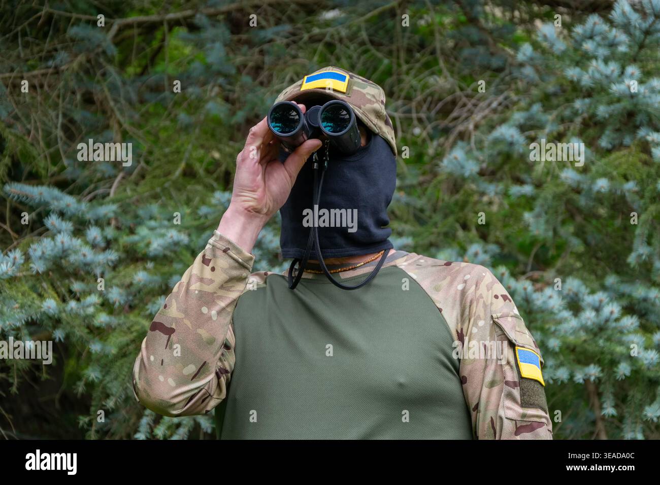 Soldato con binocoli e patch di bandiera Ucraina durante la sorveglianza. Foto Stock