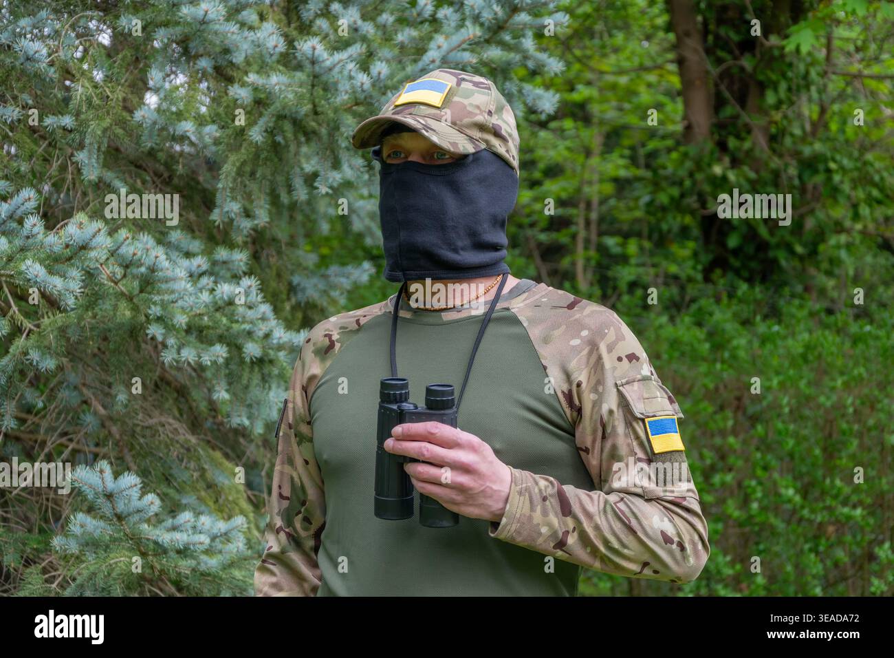 La persona in mimetismo e balaclava conduce ricognizioni, valuta le minacce e monitora un potenziale confine di conflitto Foto Stock