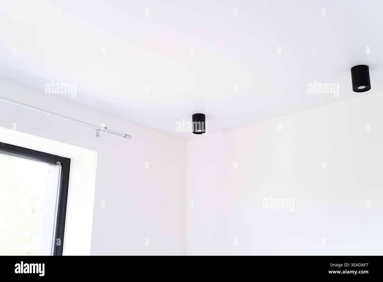 Gli interni moderni e minimalisti presentano pareti bianche, lampade a soffitto nere e una finestra con una semplice barra della tenda Foto Stock