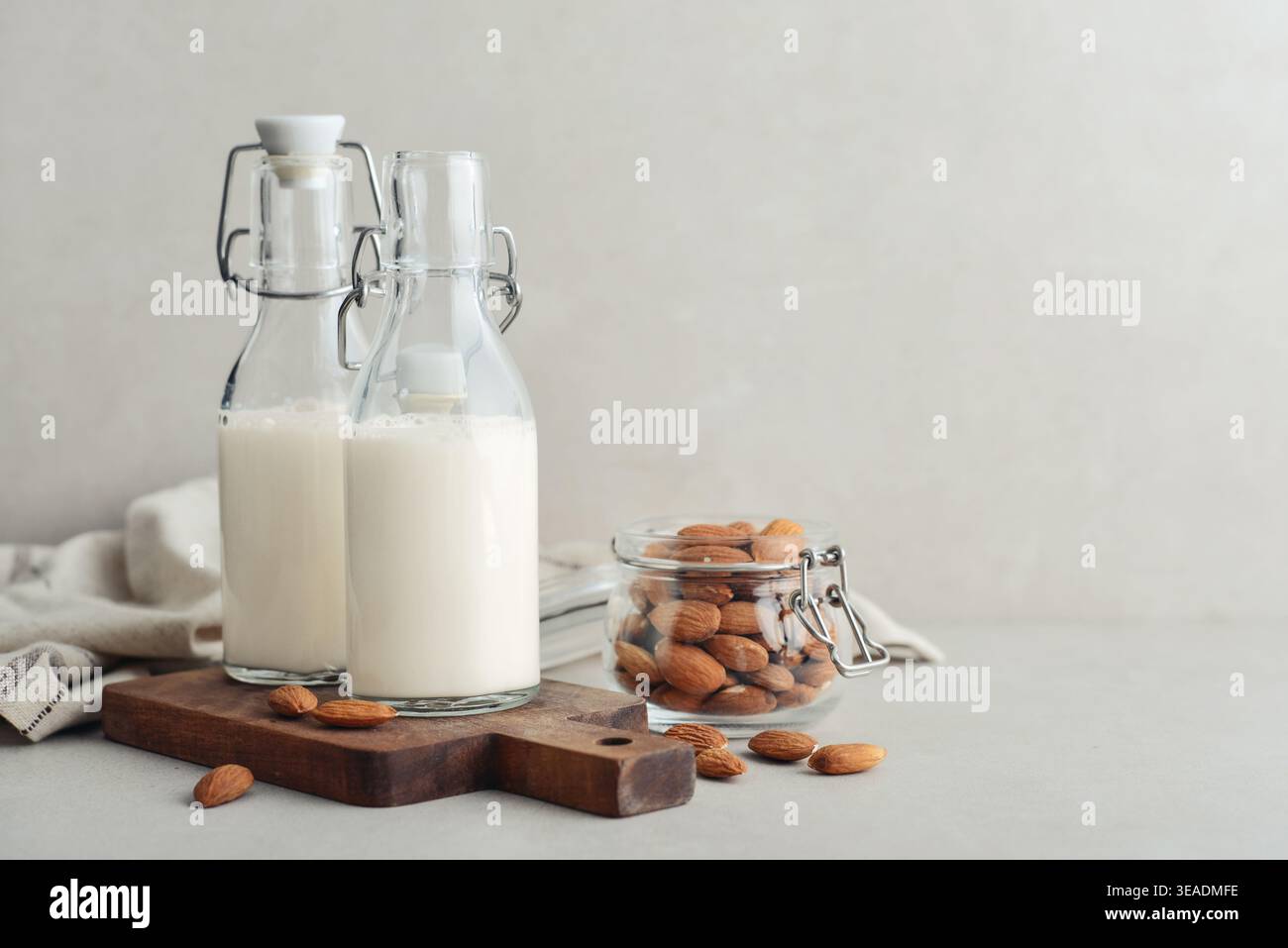 Latte di mandorla in bottiglie di vetro con noci di mandorla su sfondo chiaro Foto Stock
