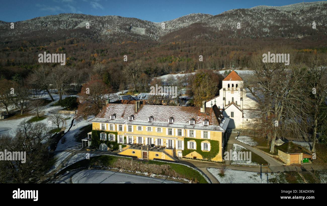 Veduta aerea di un maestoso edificio giallo con un tetto di tegole rosse, in contrasto con il paesaggio innevato e lo sfondo delle montagne, Chéser Foto Stock