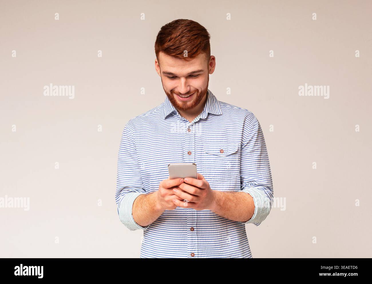 Giovane uomo absorbedly la messaggistica di testo sul suo cellulare Foto Stock