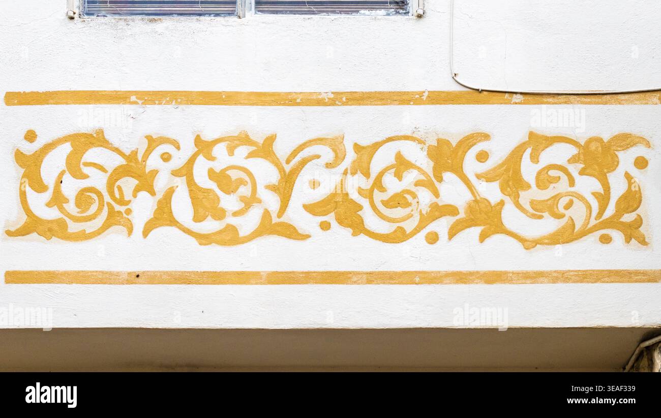 Murale ornamentale con motivi floreali dorati su parete in stucco bianco con bordo decorativo a scorrimento Foto Stock