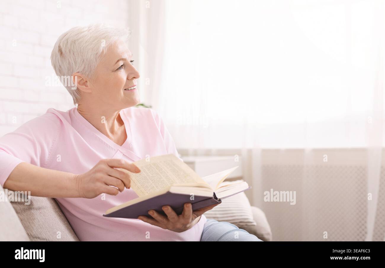 Sognante donna senior in un momento di relax a casa con il libro preferito Foto Stock