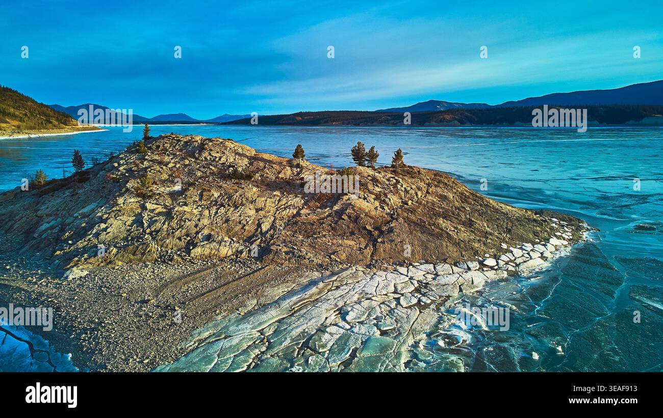 Affioramento roccioso del lago ghiacciato dall'alto e alberi di conifere nel paesaggio invernale Foto Stock