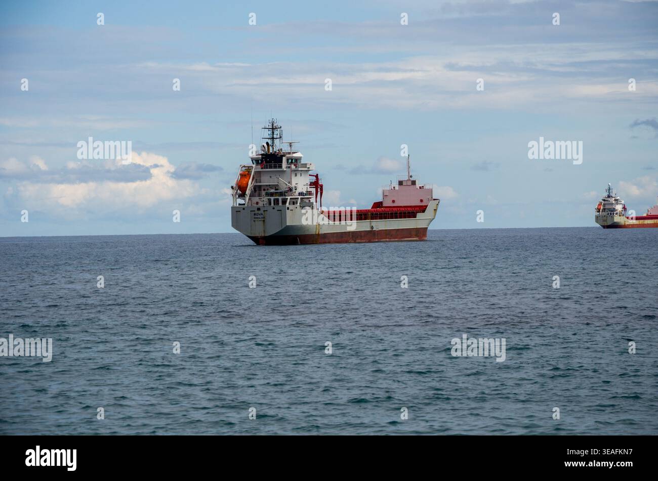 Navi da carico ancorate in un oceano calmo sotto un cielo parzialmente nuvoloso Foto Stock