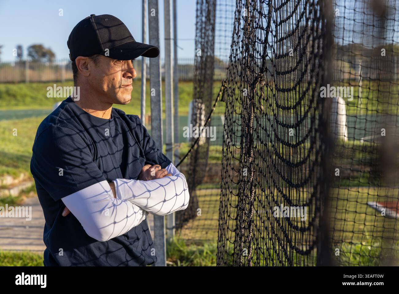 Uomo maturo in piedi a sinistra, indossa un cappellino da baseball con reti e pali sul campo, copia spazio Foto Stock