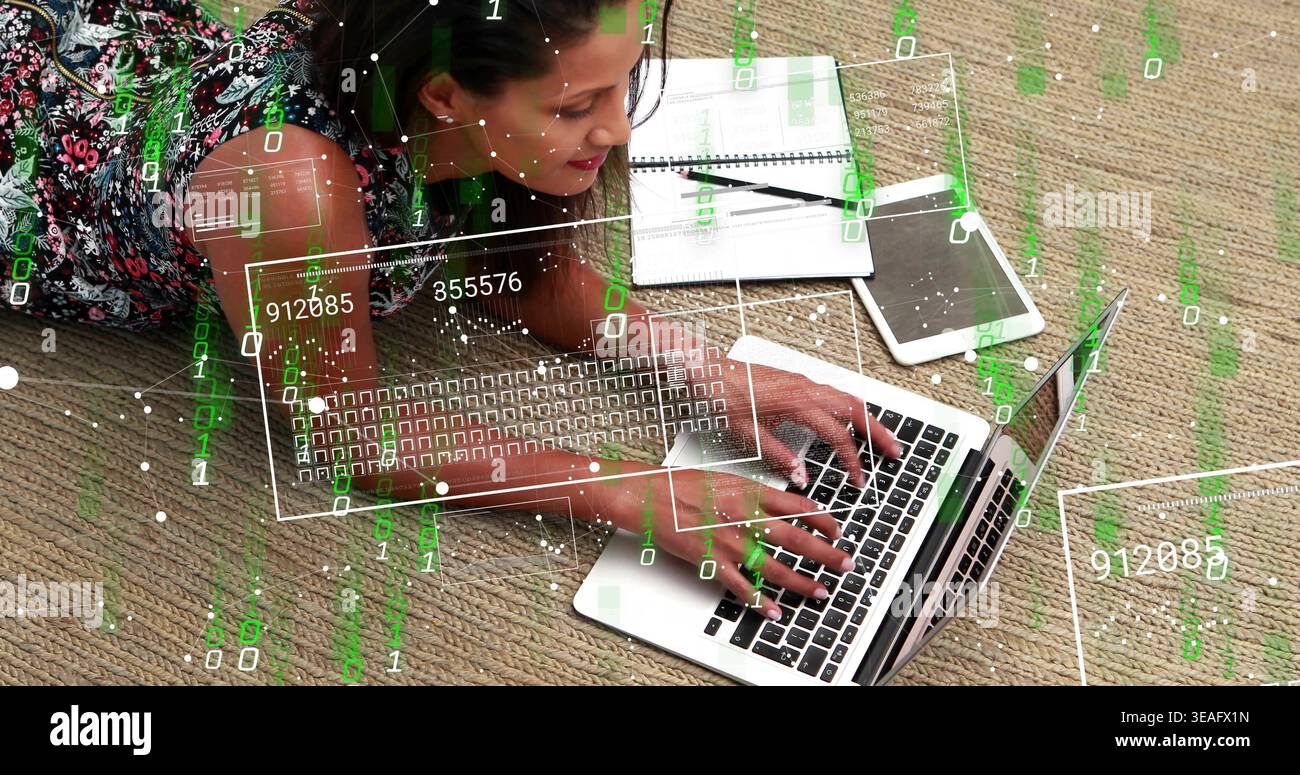 Donna che scrive a casa su un tappeto, indossa un abito floreale, utilizza un notebook argentato con un'interfaccia utente verde Foto Stock