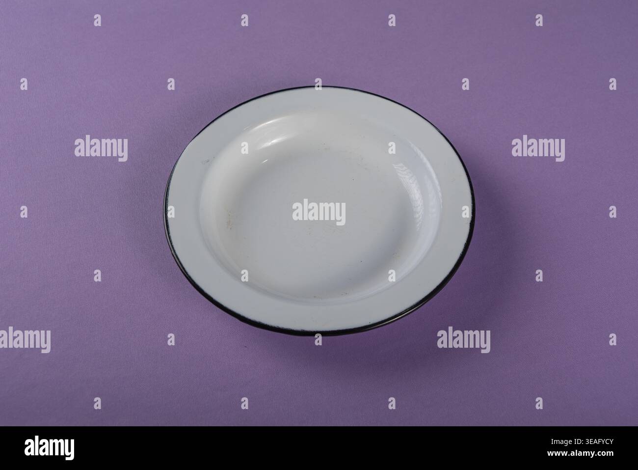 Composizione minimalista della piastra in smalto bianco su una superficie viola chiaro. L'illuminazione pulita da studio mette in risalto texture e forme. Utile per mangiare sano o Foto Stock