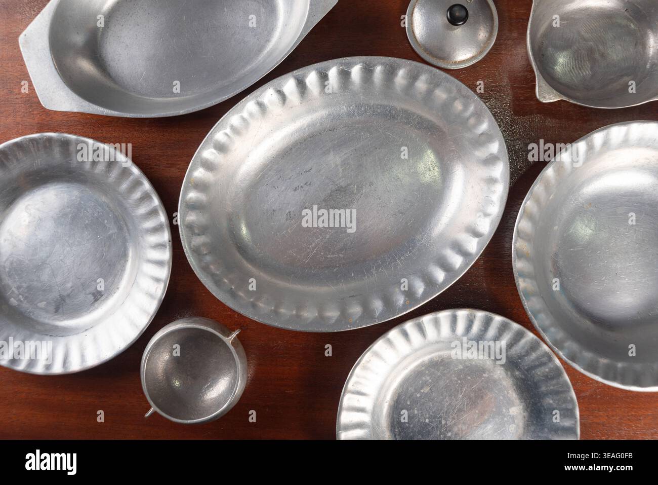 Colpo d'occhio di peltro che serve piatti, piatti e ciotole su un tavolo di legno scuro. La luce soffusa da studio mette in risalto le texture. Adatto per l'arredamento vintage, Foto Stock