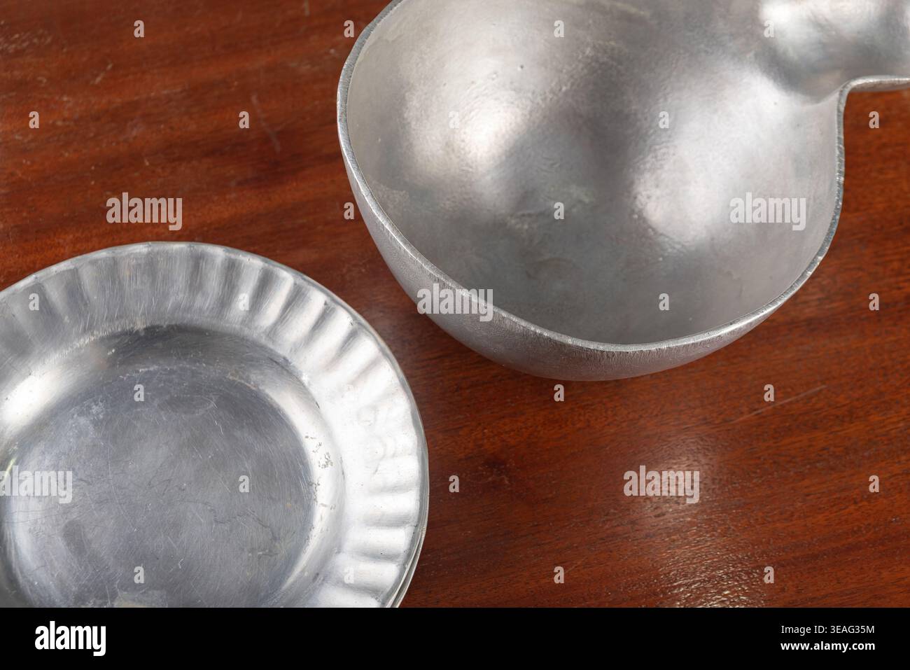 Natura morta con antichissima ciotola di peltro e piccolo piatto su una ricca superficie di legno. L'illuminazione soffusa e diffusa migliora le texture. Ideale per vintage e rustici Foto Stock